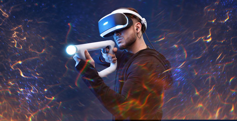 Obraz na płótnie Canvas Beautiful man over dark magic background. Gamer guy in glasses of virtual reality with controllers in hands. Augmented reality, game, hobby concept. VR. Blue neon light.