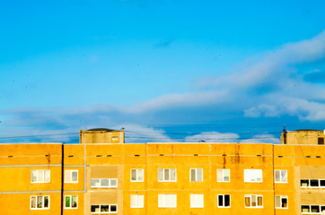 Bright yellow 9-storey building on a background of bright saturated blue sky.