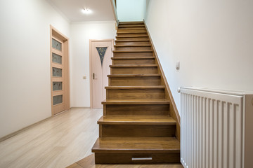 Interior of a house or appartment hallway with oak wooden stairs and room doors.