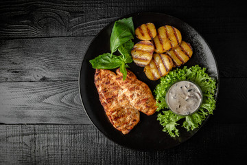 Grilled chicken fillet with homemade potatoes and sauce. Black boards background