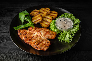Grilled chicken fillet with homemade potatoes and sauce. Black boards background