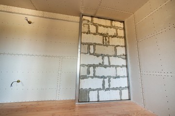 Unfinished brick wall in a room under construction prepared for drywall plates frame installation.