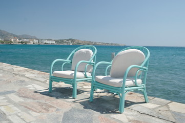 Fototapeta na wymiar wooden turquoise chairs with soft cushions stand on the waterfront next to the blue sea