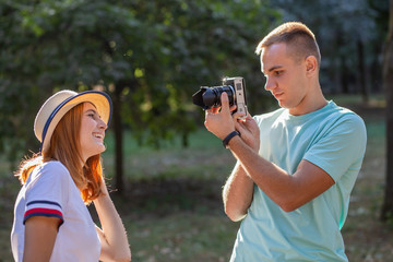 Young teenage couple taking pictures of one another outdoors in sunny summer park.