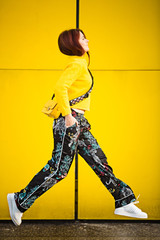 Joyful happy young woman jumping against yellow wall in city. Outdoors lifestyle portrait of student girl jumping.