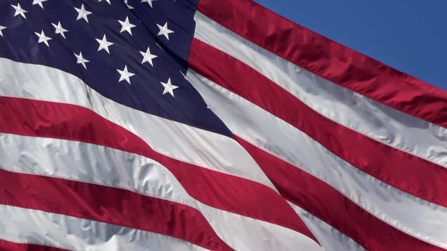 4K. American flag waving in the wind on flagpole in the city of Los Angeles with clear sky and cloudy background. Close up of a cloth sill flag fluttering through the air. Cinema effect.