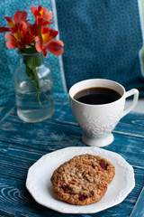 Oatmeal cookies, black coffee and a bouquet of red flowers stand on a tray in bed.