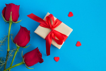 Gift with red bow, red roses and red  hearts on the blue background. Top view. Copy space.