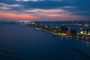 Aerial night panorama of Limassol, Cyprus waterfront. Famous mediterranean city resort in evening with Molos Park, promenade or embankment and buildings, from above view.
