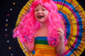 Happy Cute caucasian boy changed clothes at carnival in dress of girl of rainbow color. Pink doll wig. LGBT color background. Education in kindergarten and preschool children. hair coloring