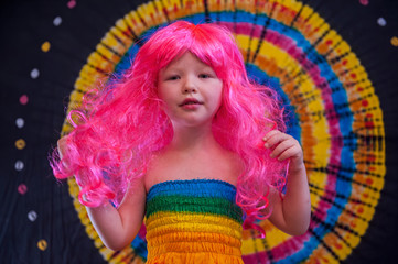 Happy Cute caucasian boy changed clothes at carnival in dress of girl of rainbow color. Pink doll wig. LGBT color background. Education in kindergarten and preschool children. hair coloring