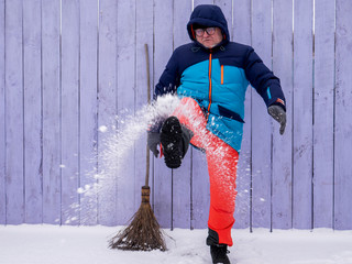 man in bright ski suit stands holding broom in his hands and is going to clean the snow in winter...