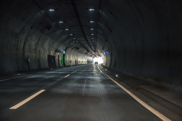 Fahrt durch einen dunklen Tunnel einer Autobahn mit Sicht auf das Licht am Ende des Tunnels