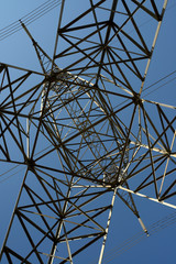 Abstract latticework under a steel suspension electric tower with high tension power lines and a blue sky