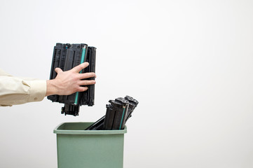 Male hands of an office worker stack spent cartridges in a bucket against a white wall.