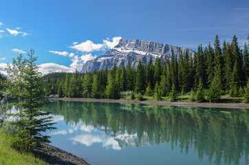Peak of Mt. Rundle with snow bands reflected in tree lined Cascade Pond in Banff National Park, Alberta, Canada