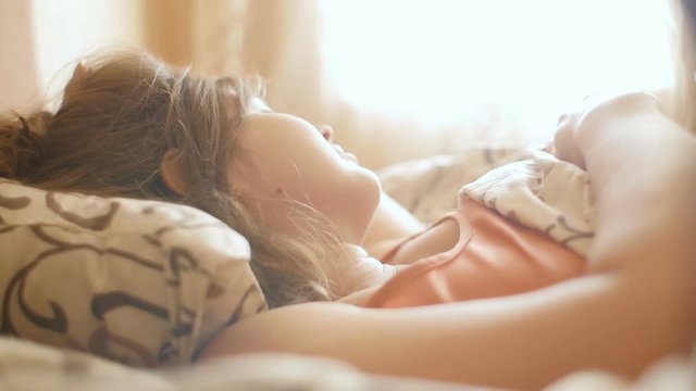 beautiful young woman basking in bed in the sunshine of the morning sun, the girl woke up and enjoying new day, lazy to get up, the concept of lifestyle and rest