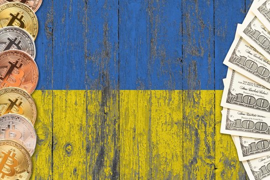 Ukraine savings concept. Bitcoins and dollar banknotes on the side of national flag with wooden background. Trading currencies. - Powered by Adobe