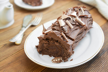 Chocolate swiss roll isolated on a wooden background. Chocolate sweet dessert. Pastry for breakfast or tea.