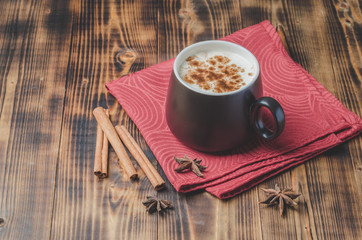 Eggnog. Traditional christmas cocktail in a black mug on a red napkin with cinnamon sticks and anise on wooden table.