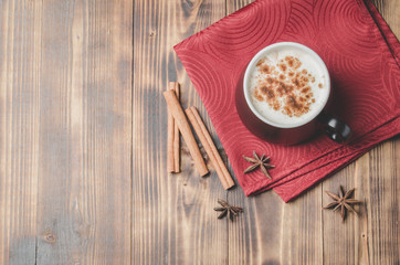 Eggnog. Traditional christmas cocktail in a black mug on a red napkin with cinnamon sticks and anise on wooden table. Top view and copyspace.