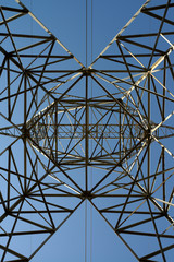 Abstract latticework looking up a steel suspension electric tower with high tension power lines and a blue sky
