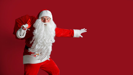 Fototapeta na wymiar Portrait of surprised crouching Santa Claus carrying huge red sack with presents on red studio background. Isolate.
