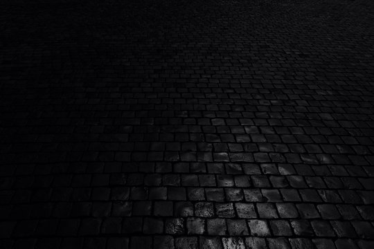 Black background. Old cobblestone pavement in perspective. Abstract background. Black and white photo.