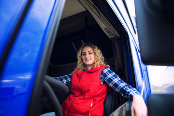 Shot of woman driver sitting in truck cabin. Female trucker ready for a drive. Truck driver...