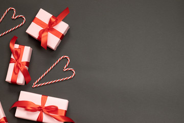 Festive composition of gift boxes with red ribbons decor, candy cane on a dark background with place for text. Top view flat top view