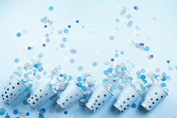 Beautiful festive cups in a row with colorful confetti on blue pastel background. Flat lay style. Place for text.