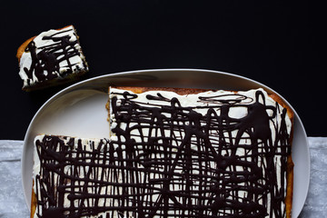 A cake with cream and chocolate photographed from above with a cut piece against a dark background