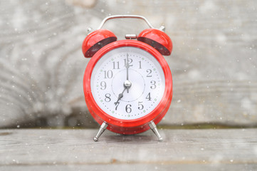 Vintage red clock and alarm clock in centre on wooden background. falling snow