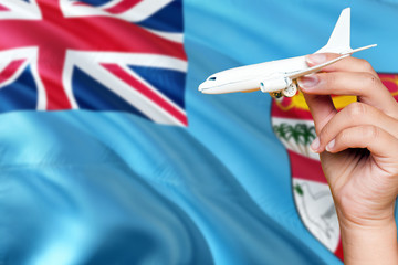 Fiji travel concept. Woman holding a miniature plane on national flag background. Holiday and voyage theme with copy space for text.