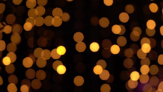 Defocused glowing golden lights of led holiday garlands shining in darkness of night. Abstract festive background. Real time 4k video footage.