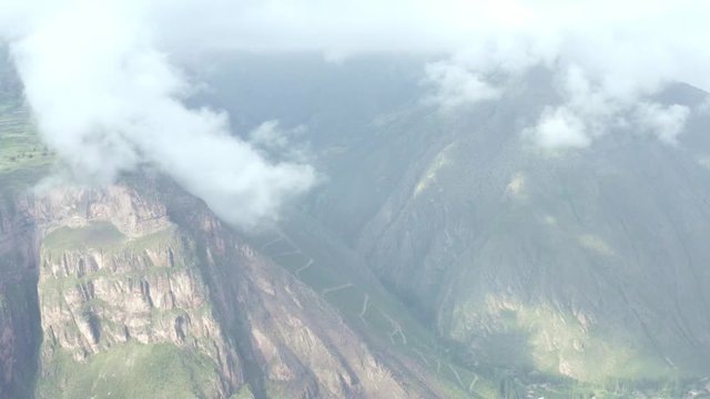 Panning over 400 meters high towards mountains with fields, rocks, clouds, road.