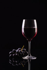 A glass of wine on a black background with grapes. Aromatic wine. Strict style. Wine on the dark