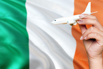 Ireland travel concept. Woman holding a miniature plane on national flag background. Holiday and voyage theme with copy space for text.