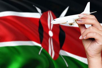 Kenya travel concept. Woman holding a miniature plane on national flag background. Holiday and voyage theme with copy space for text.