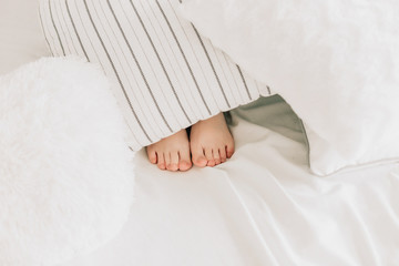 Under the white covers with feet showing in a bed