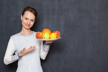 Portrait of happy cheerful young woman pointing at plate with fruits