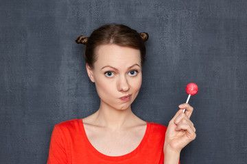 Obraz premium Portrait of thoughtful blond girl holding pink lollipop in one hand
