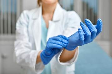 Close up of a female doctor putting a blue latex gloves on a clinic background. - obrazy, fototapety, plakaty