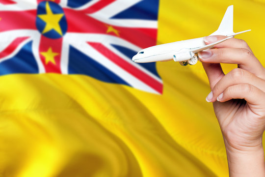 Niue Travel Concept. Woman Holding A Miniature Plane On National Flag Background. Holiday And Voyage Theme With Copy Space For Text.