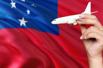 Samoa travel concept. Woman holding a miniature plane on national flag background. Holiday and...