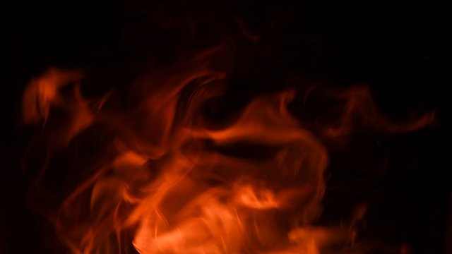 Fire flames with flying sparks on a black background. Firestorm texture. Bokeh lights on black background, shot of flying fire sparks in the air. Sparks from bonfire over dark night background. 4K UHD