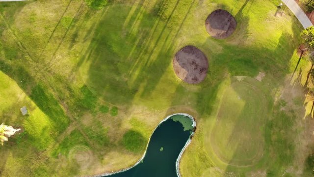4K aerial footage of golf course. Cinematic top view shot with green grass, ponds, watercourses, palm trees, patches, holes, flags. Drone flies along the field during sunset. Vacation video concept