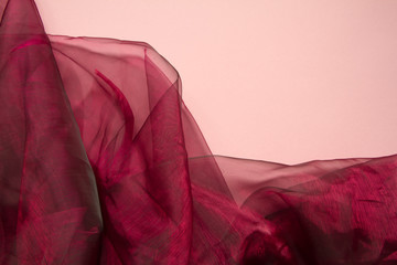 Falds of red fabric tulle or organza on a coral color background, selective focus