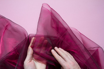 Top view of male hands holding a purple tulle or organza on a pink background, selective focus