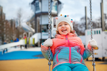 Adorable little girl on the playground. Toddler having fun on a swing on beautiful winter day